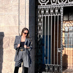 Woman in a gray spring suit standing in front of a decorative metal gate.