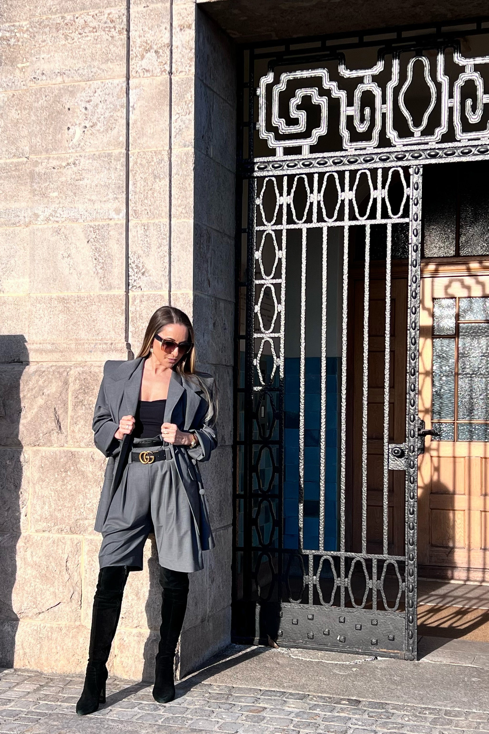 Woman in a gray spring suit standing in front of a decorative metal gate.