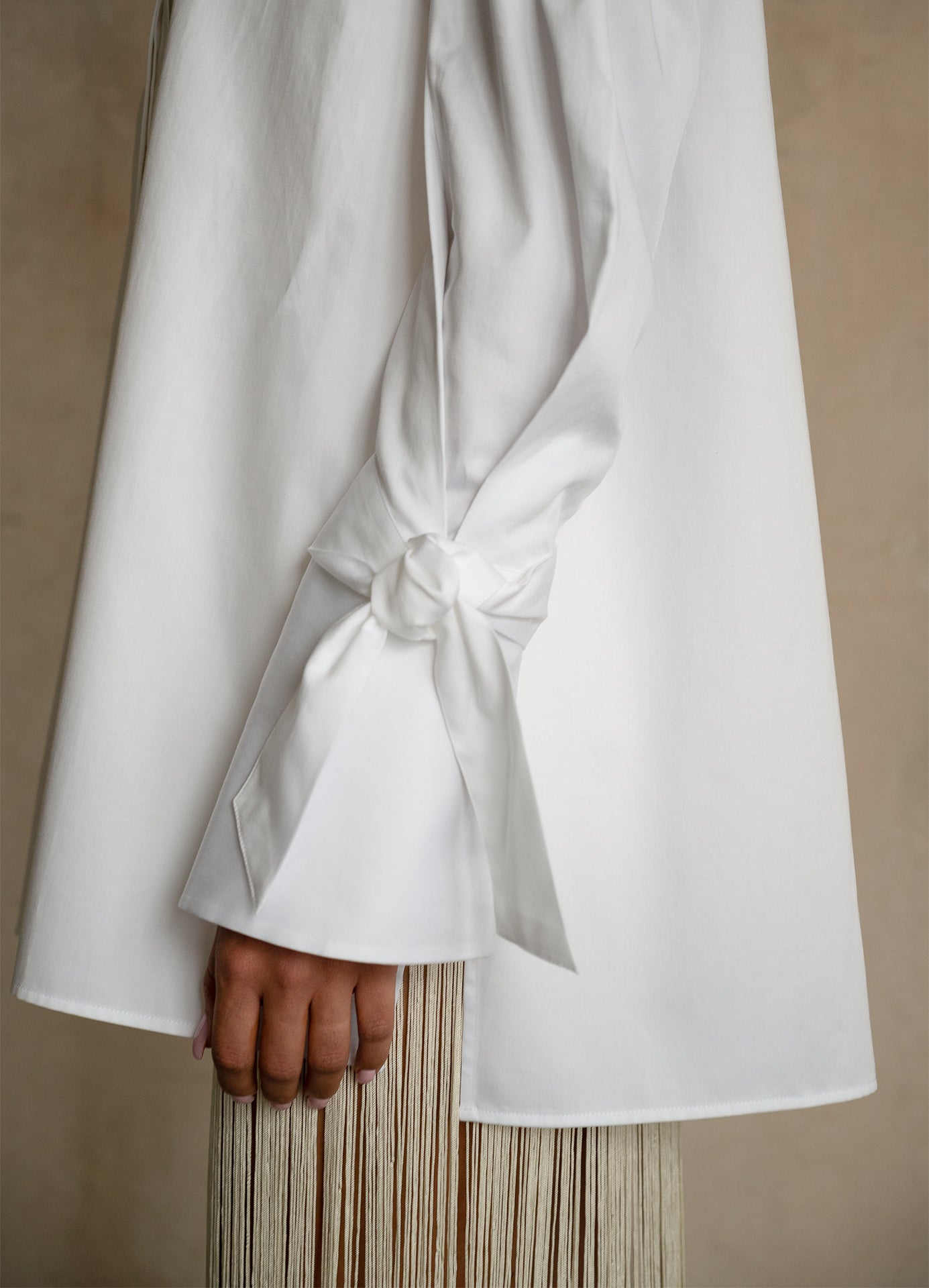 Adjustable ribbon cuff on a white gabardine shirt with extended sleeve and refined structured drape, detail view