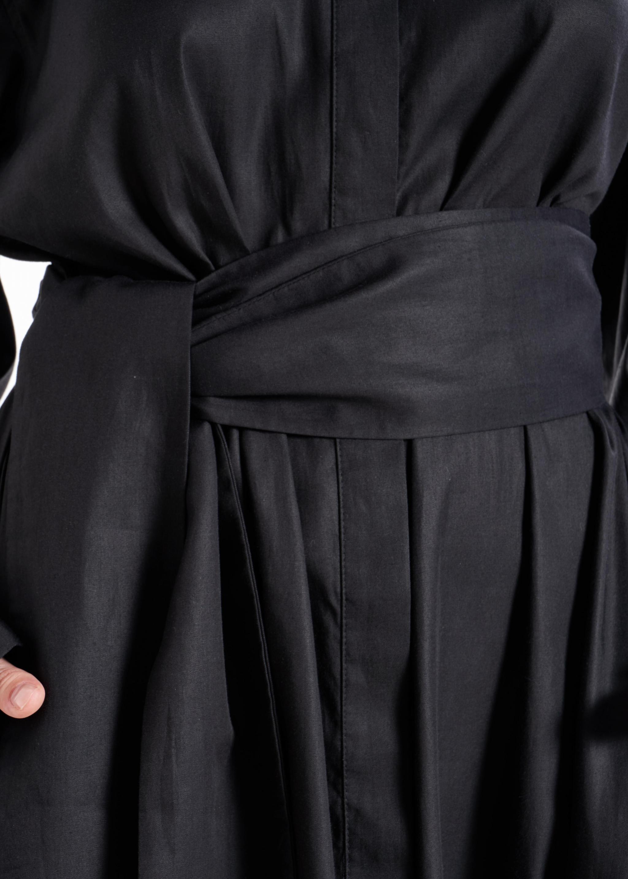 Close-up of the matching fabric belt and front fastening detail on the black shirt dress worn by a model