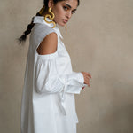 Cold-shoulder white cotton gabardine shirt with voluminous puff sleeves and ribbon cuffs, worn by a model