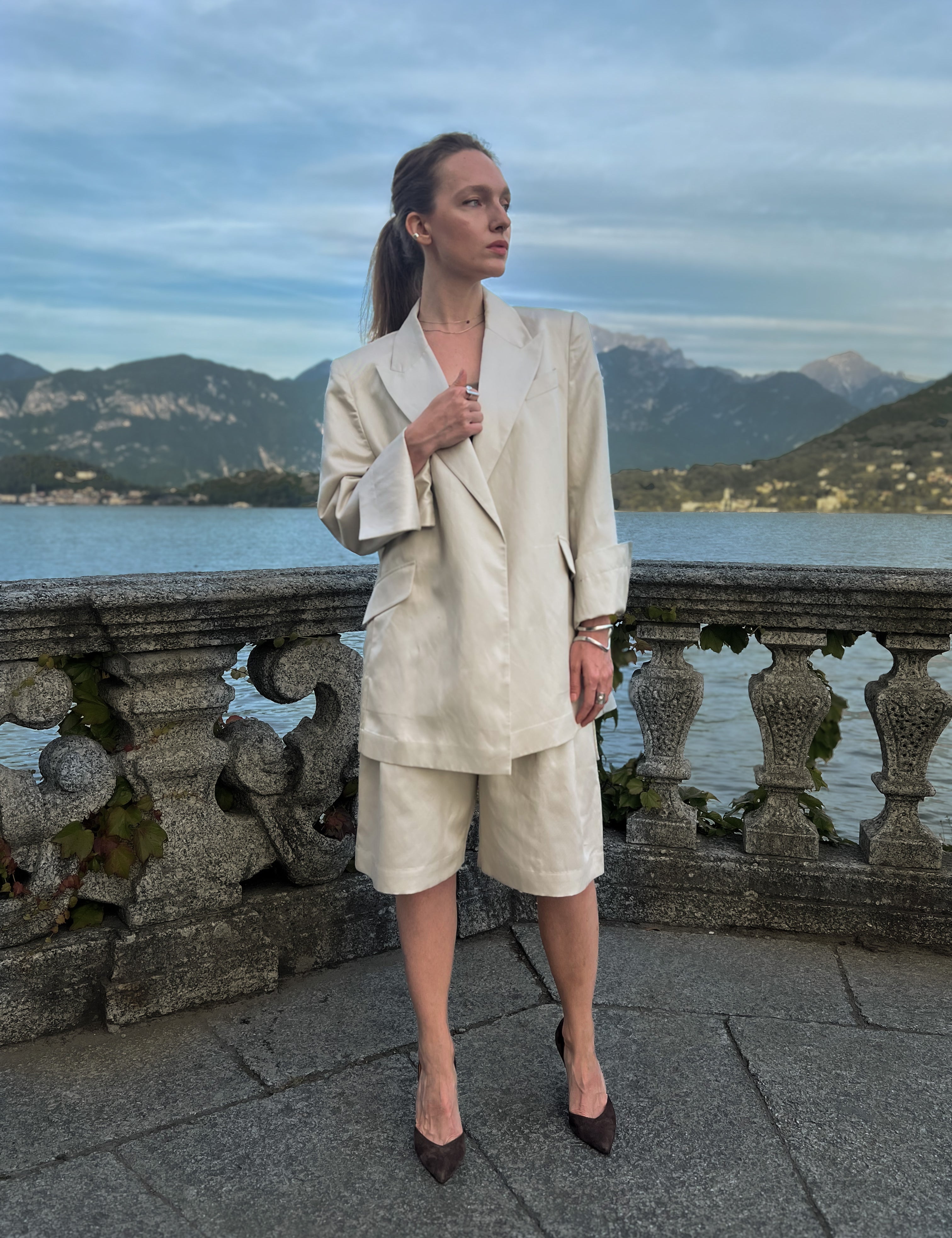 Linen-blend Bermuda shorts with front pleats and double belt loops, worn by a model on a Lake Como terrace