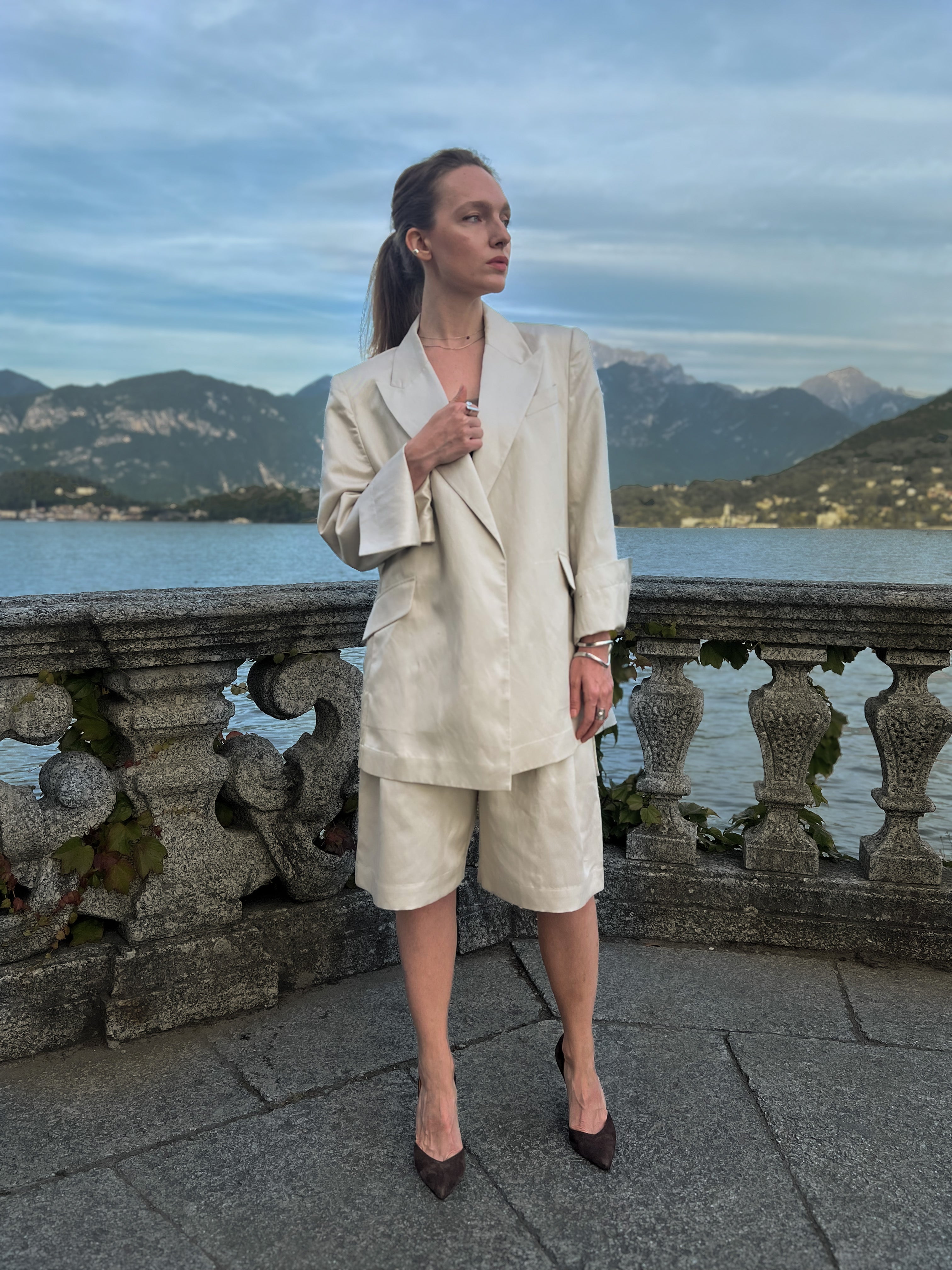 Linen-blend Bermuda shorts with front pleats and double belt loops, worn by a model on a Lake Como terrace