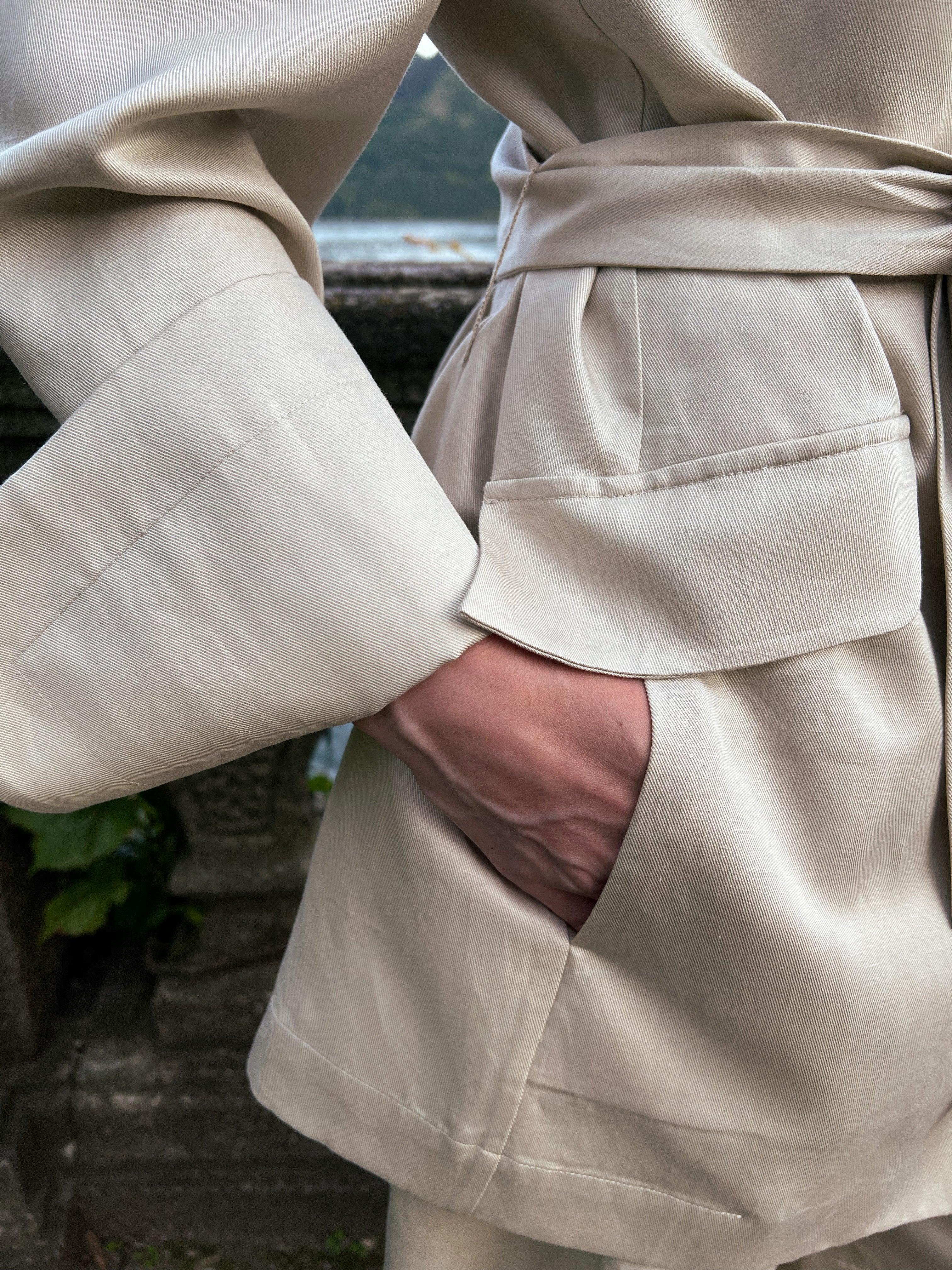 Belted linen blazer with deep flap pocket and wide turn-back cuff, close-up on a model at Lake Como