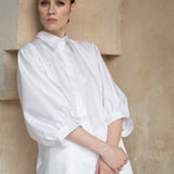 Front view of a model wearing an organic cotton white shirt with puff sleeves and a refined satin finish