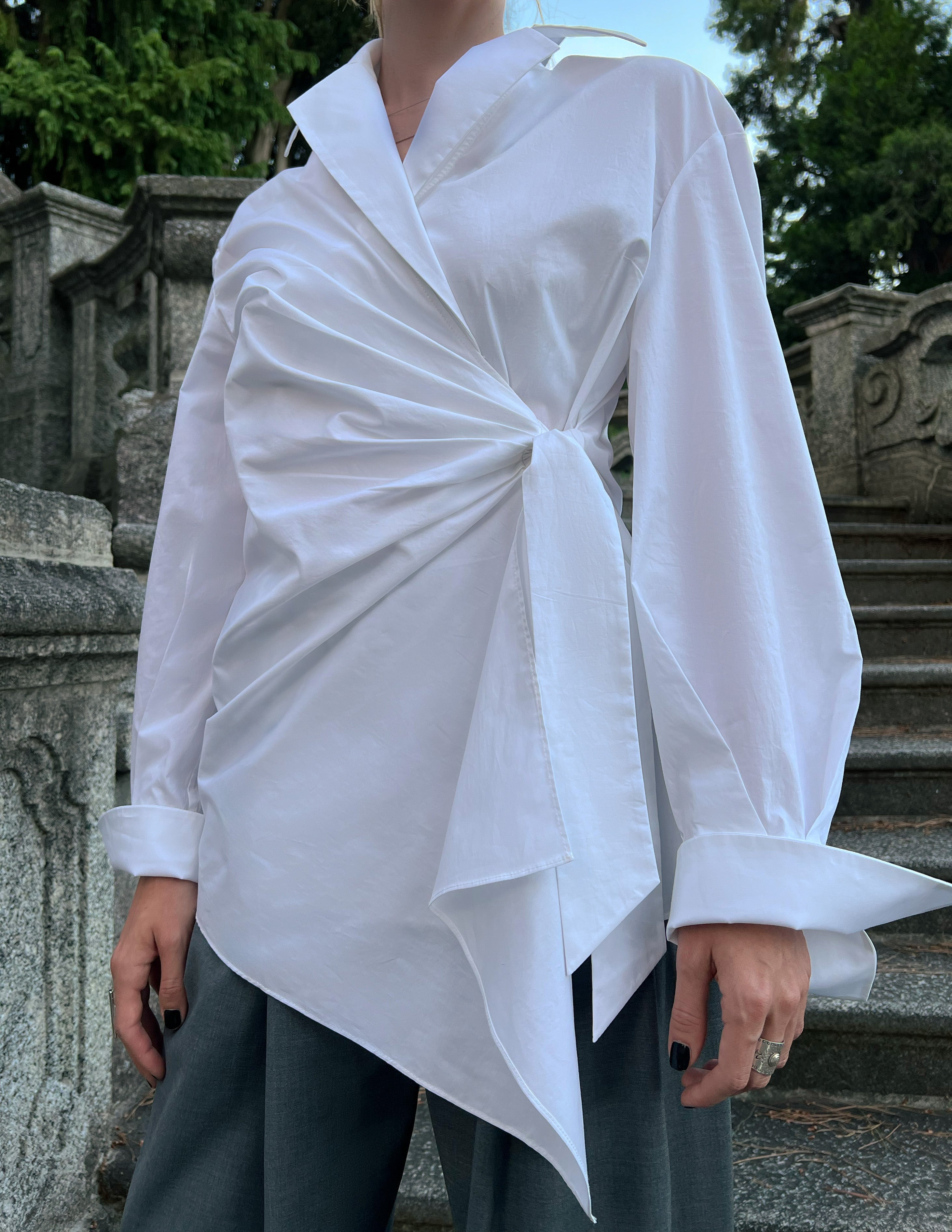 Luxury white cotton asymmetric wrap shirt worn by a model, highlighting the elegant draped front