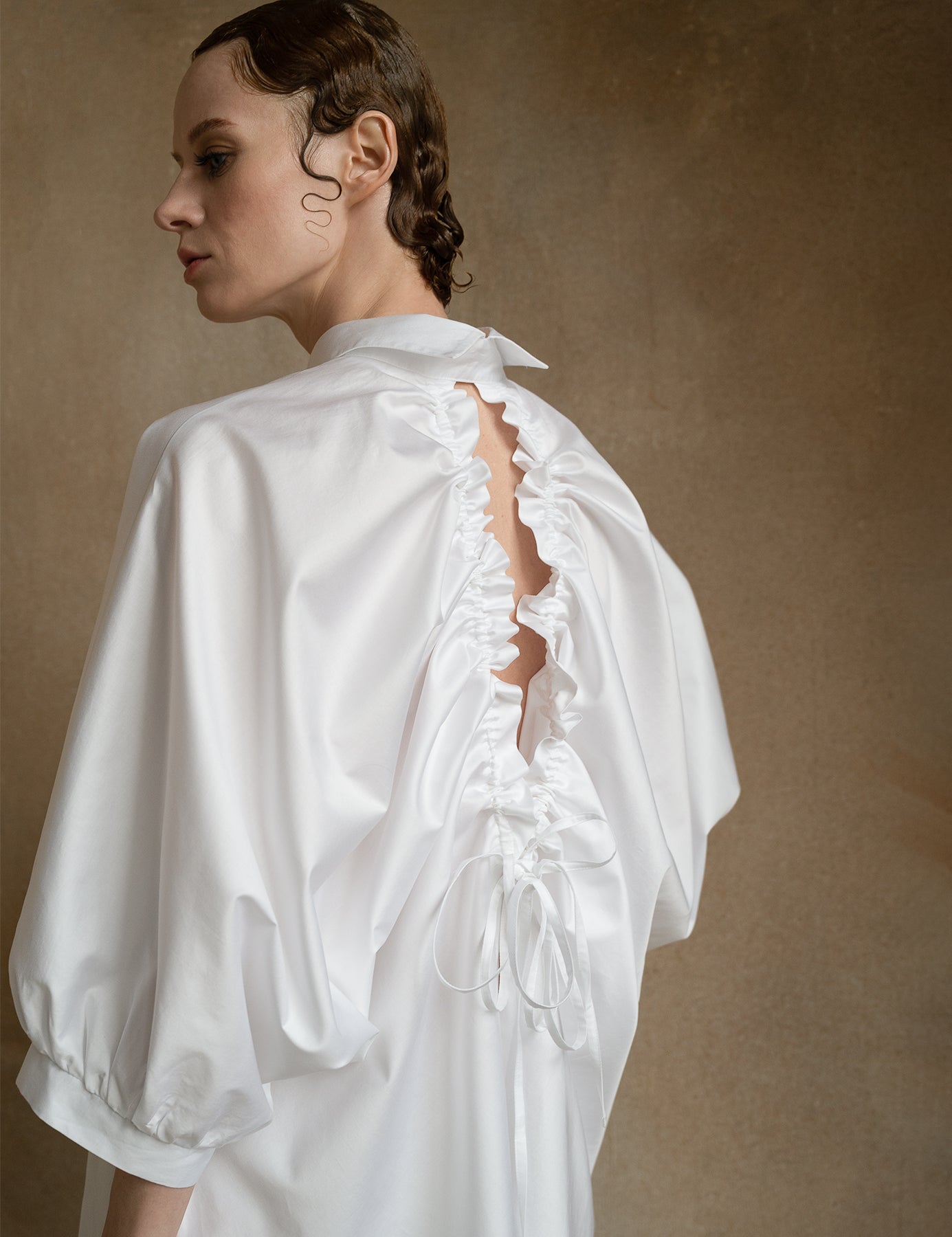 Luxury white open-back shirt worn by a model from the back, showing puff sleeves and drawstring detail