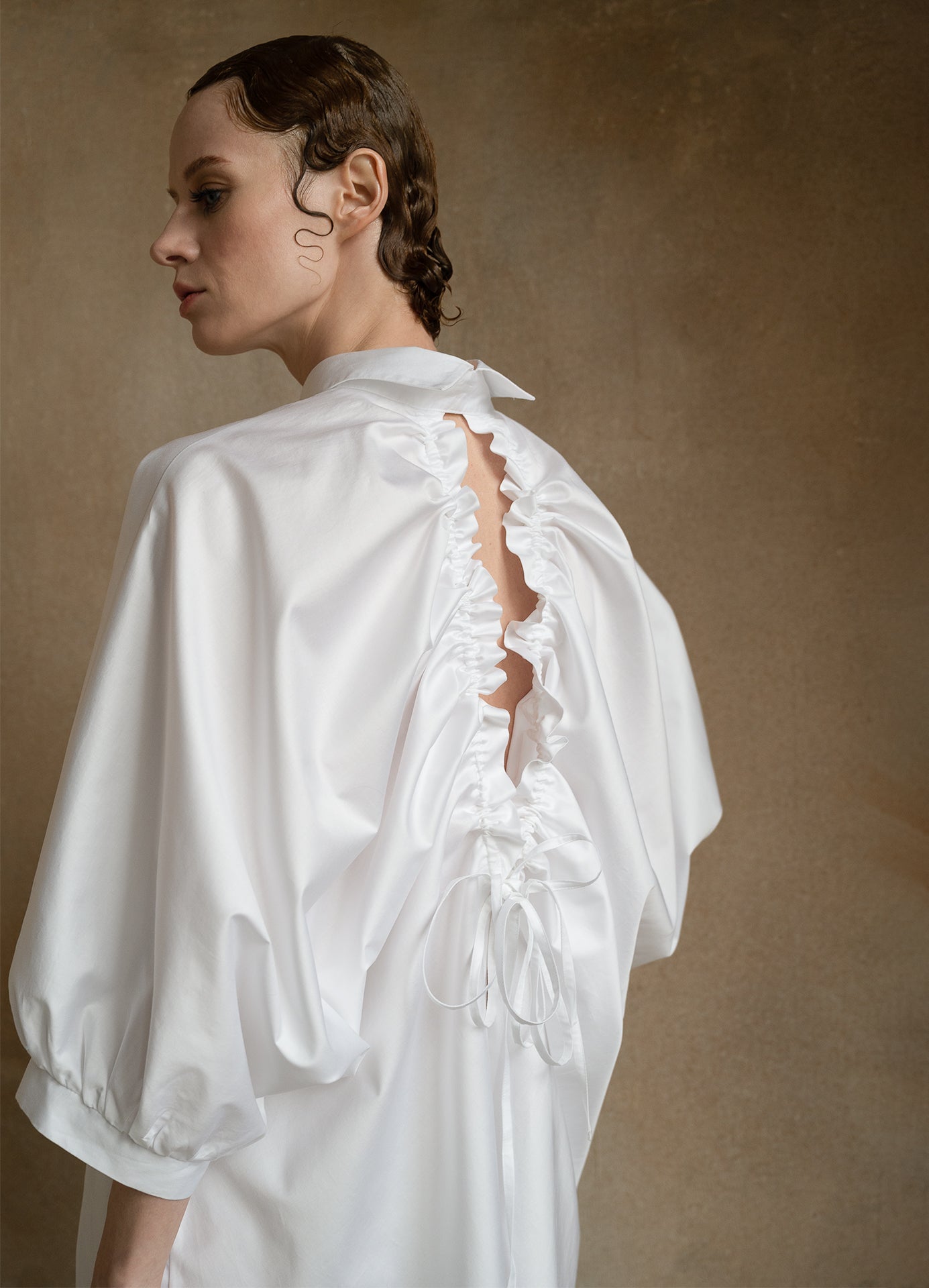 Luxury white open-back shirt worn by a model from the back, showing puff sleeves and drawstring detail