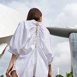 Oversized white cotton shirt worn by a model outdoors, showing the open back and adjustable drawstrings