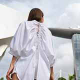 Oversized white cotton shirt worn by a model outdoors, showing the open back and adjustable drawstrings