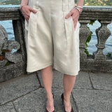 Sand linen-blend Bermuda shorts with front pleats and double belt loops, worn by a model at Lake Como, Italy