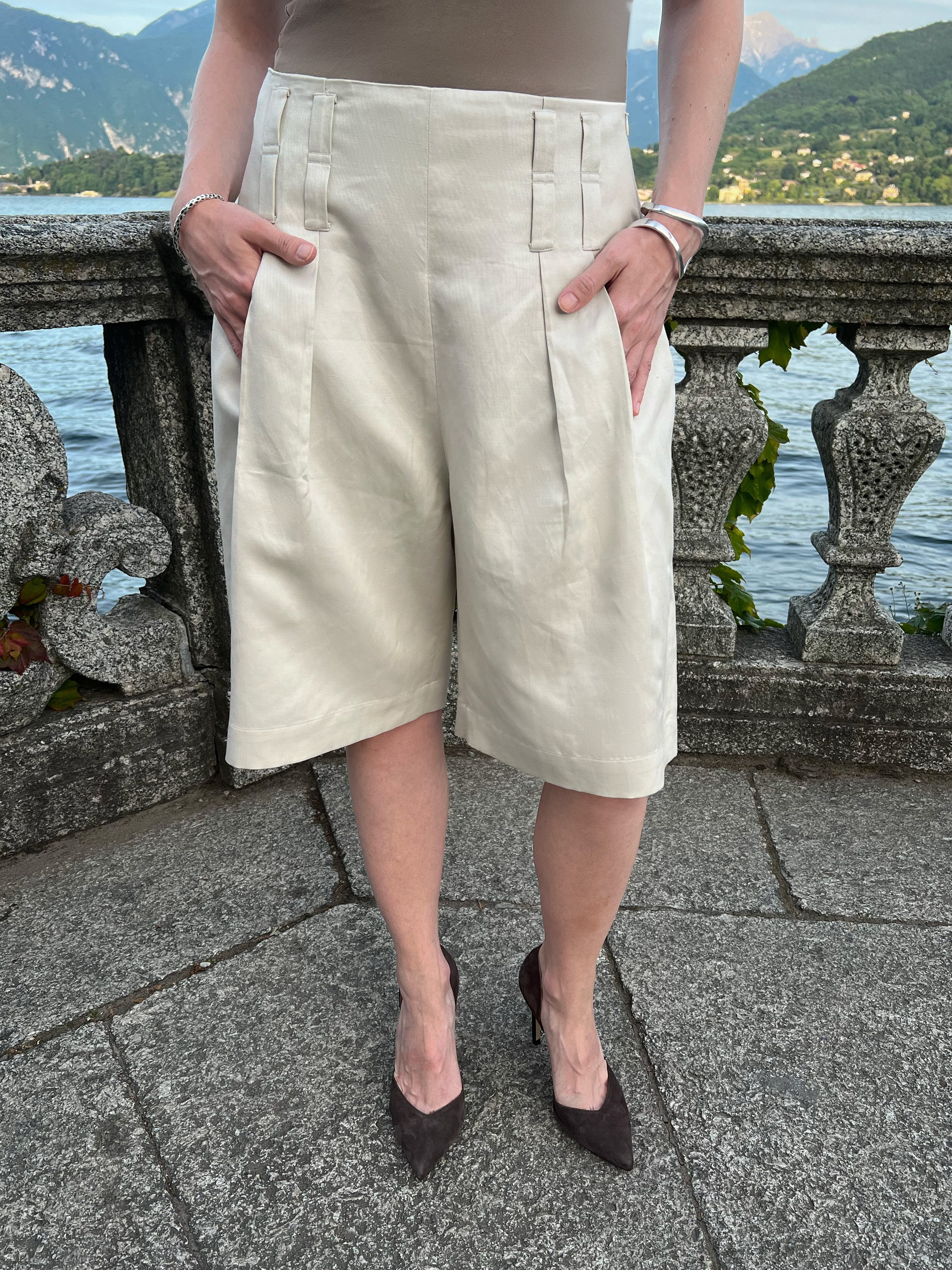Sand linen-blend Bermuda shorts with front pleats and double belt loops, worn by a model at Lake Como, Italy