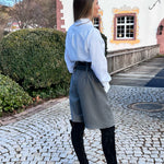 Woman standing on a cobblestone path in front of a building with a garden.