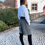 Woman standing on a cobblestone path in front of a building with a garden.