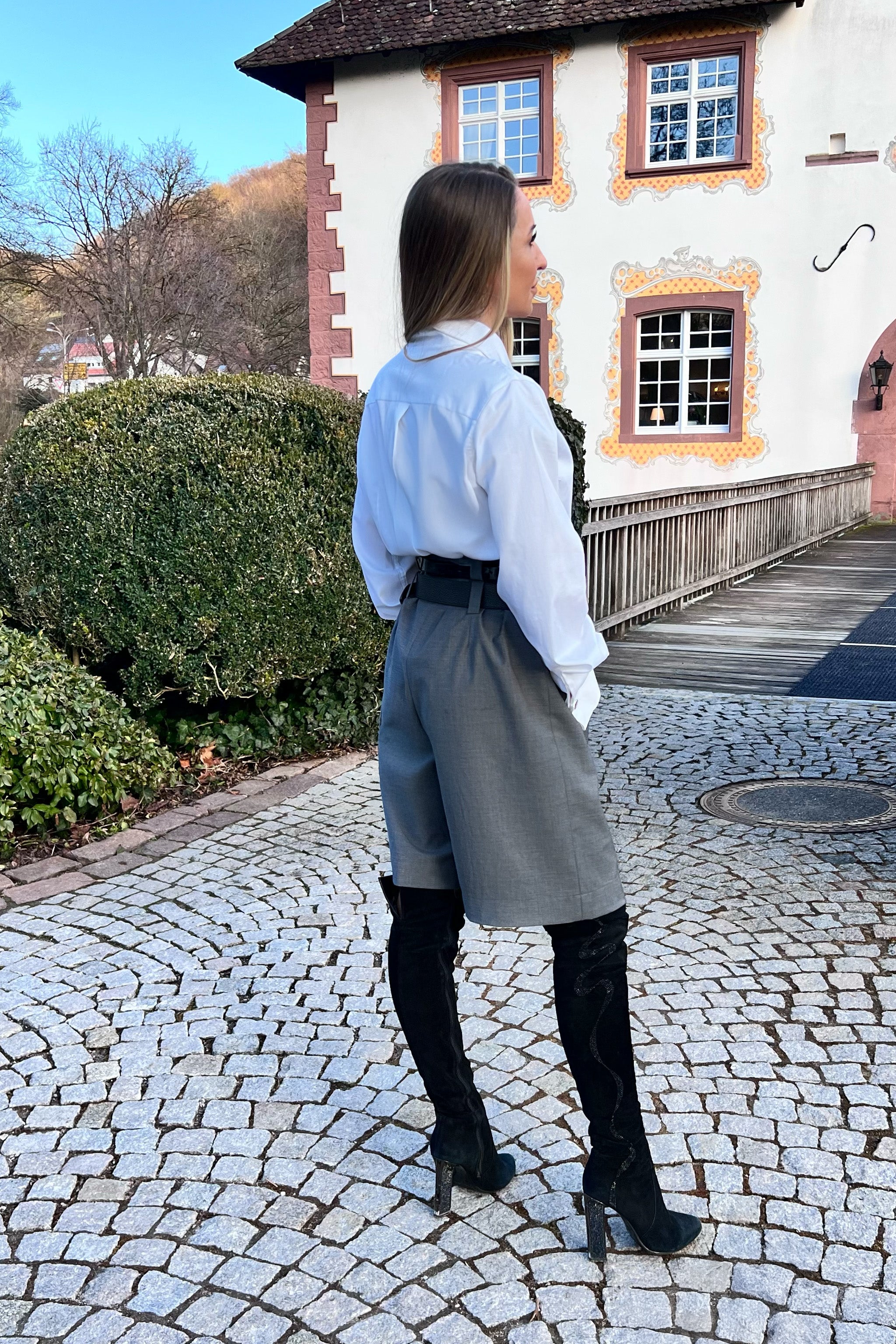 Woman standing on a cobblestone path in front of a building with a garden.