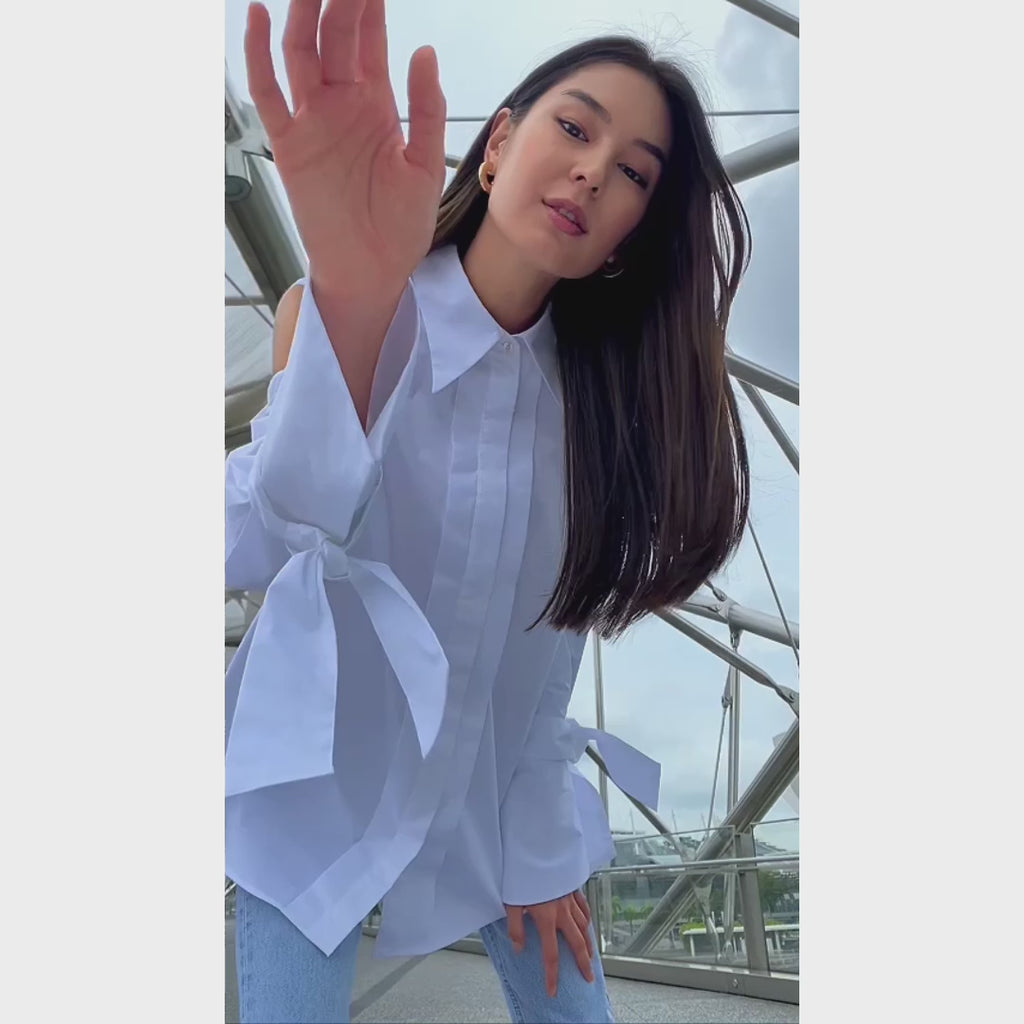 White cotton gabardine cold-shoulder shirt with voluminous puff sleeves, worn by a model in motion in Singapore