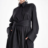 Black maxi shirt dress worn by a model with a wide waist belt, flowing silhouette and oversized cuffs