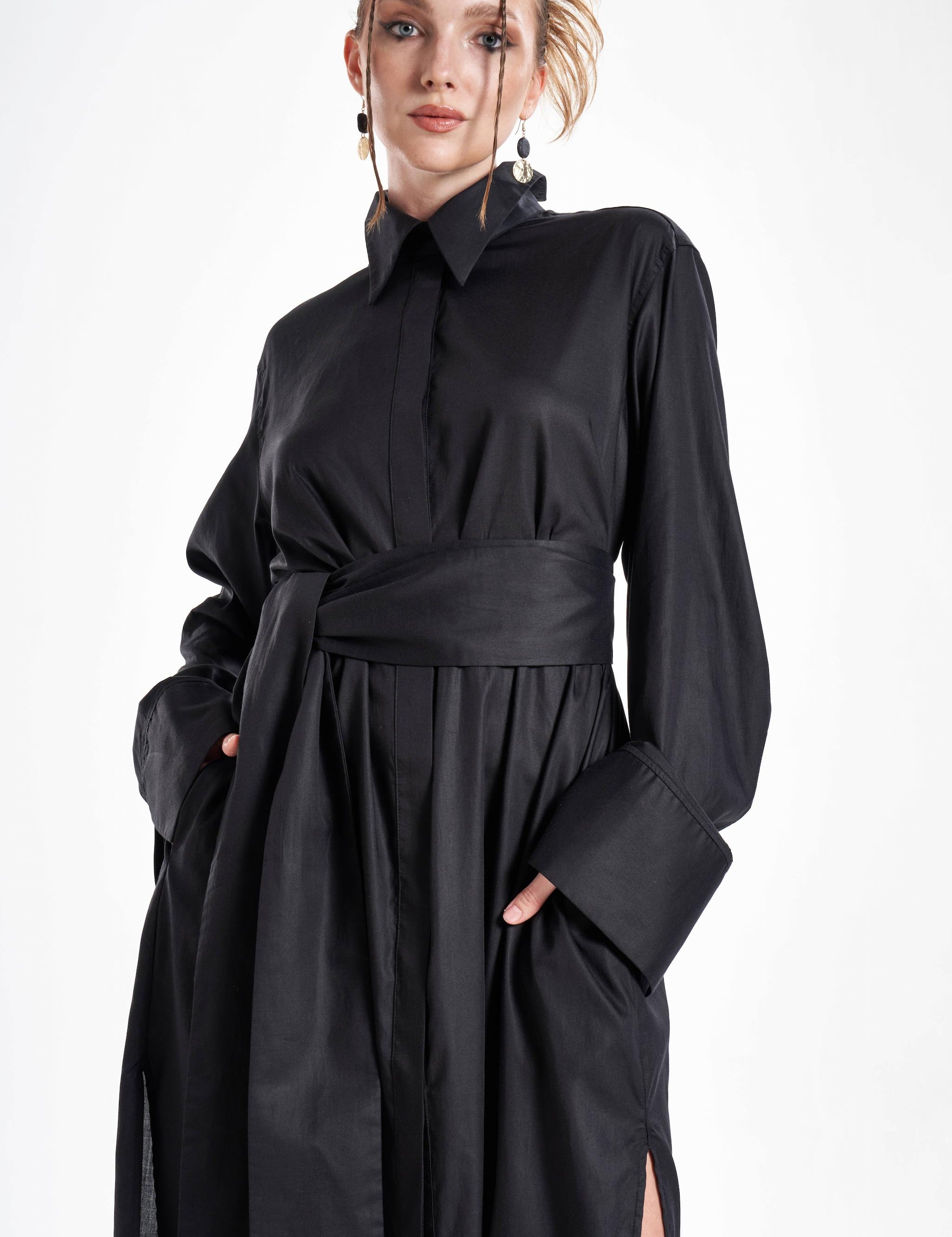 Black maxi shirt dress worn by a model with a wide waist belt, flowing silhouette and oversized cuffs