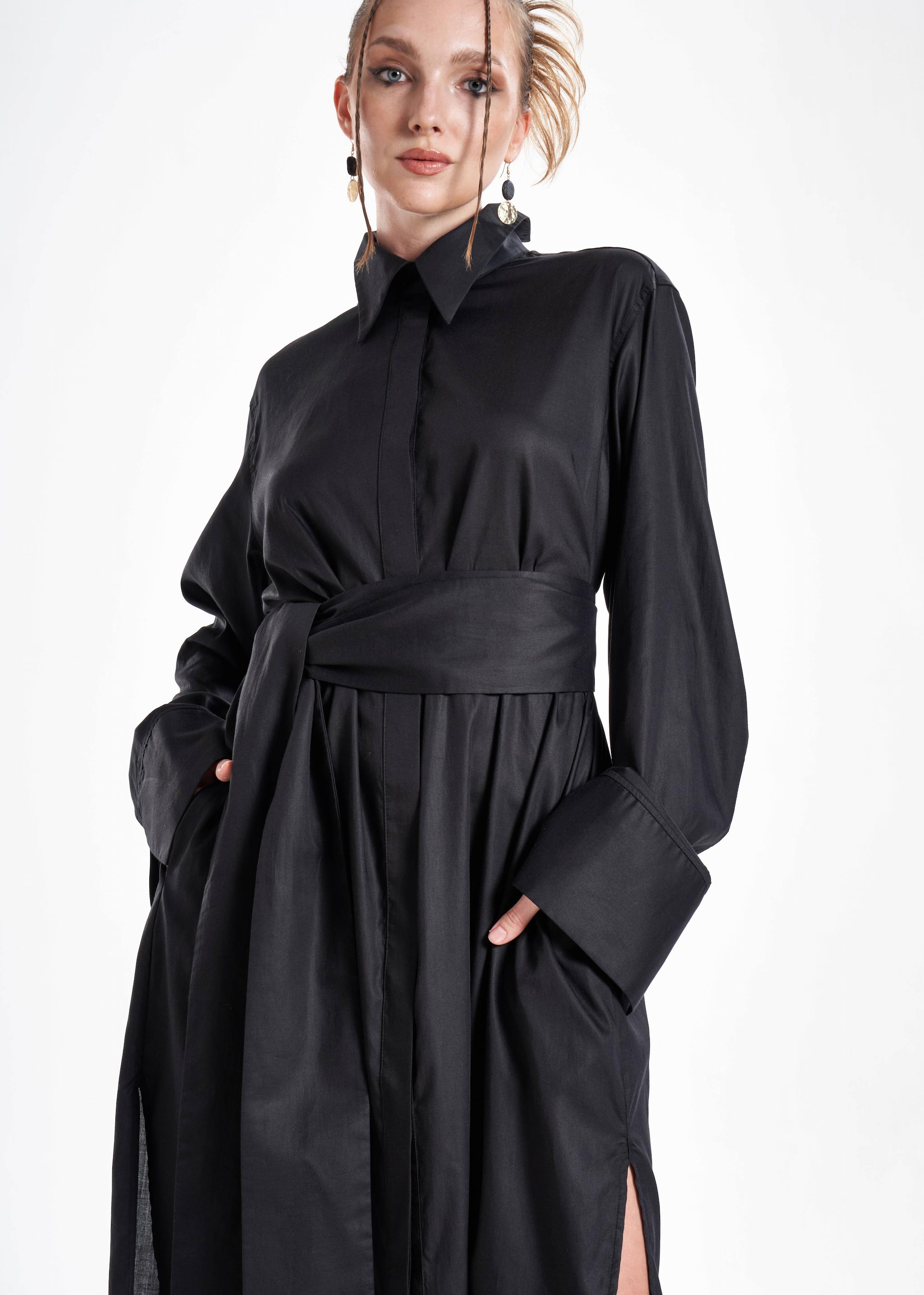 Black maxi shirt dress worn by a model with a wide waist belt, flowing silhouette and oversized cuffs