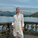 Taormina sand linen-blend blazer with self-tie waist belt and structured shoulders, worn by a model in Italy