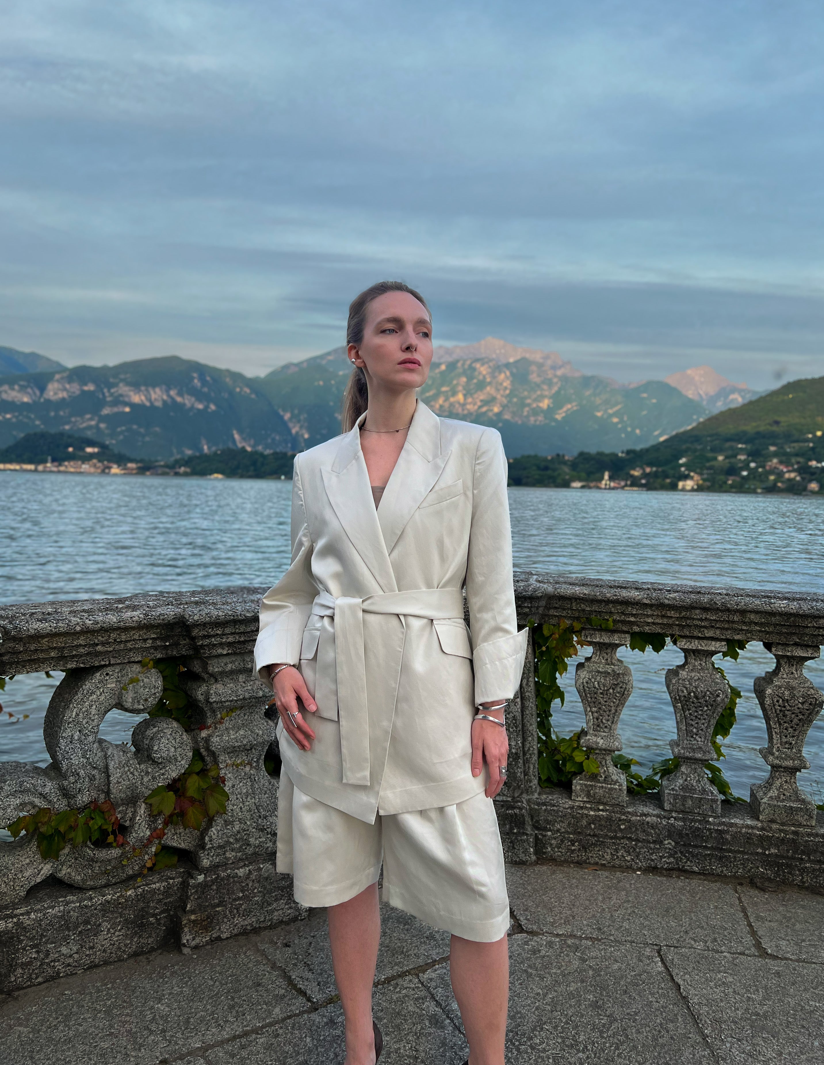 Taormina sand linen-blend blazer with self-tie waist belt and structured shoulders, worn by a model in Italy
