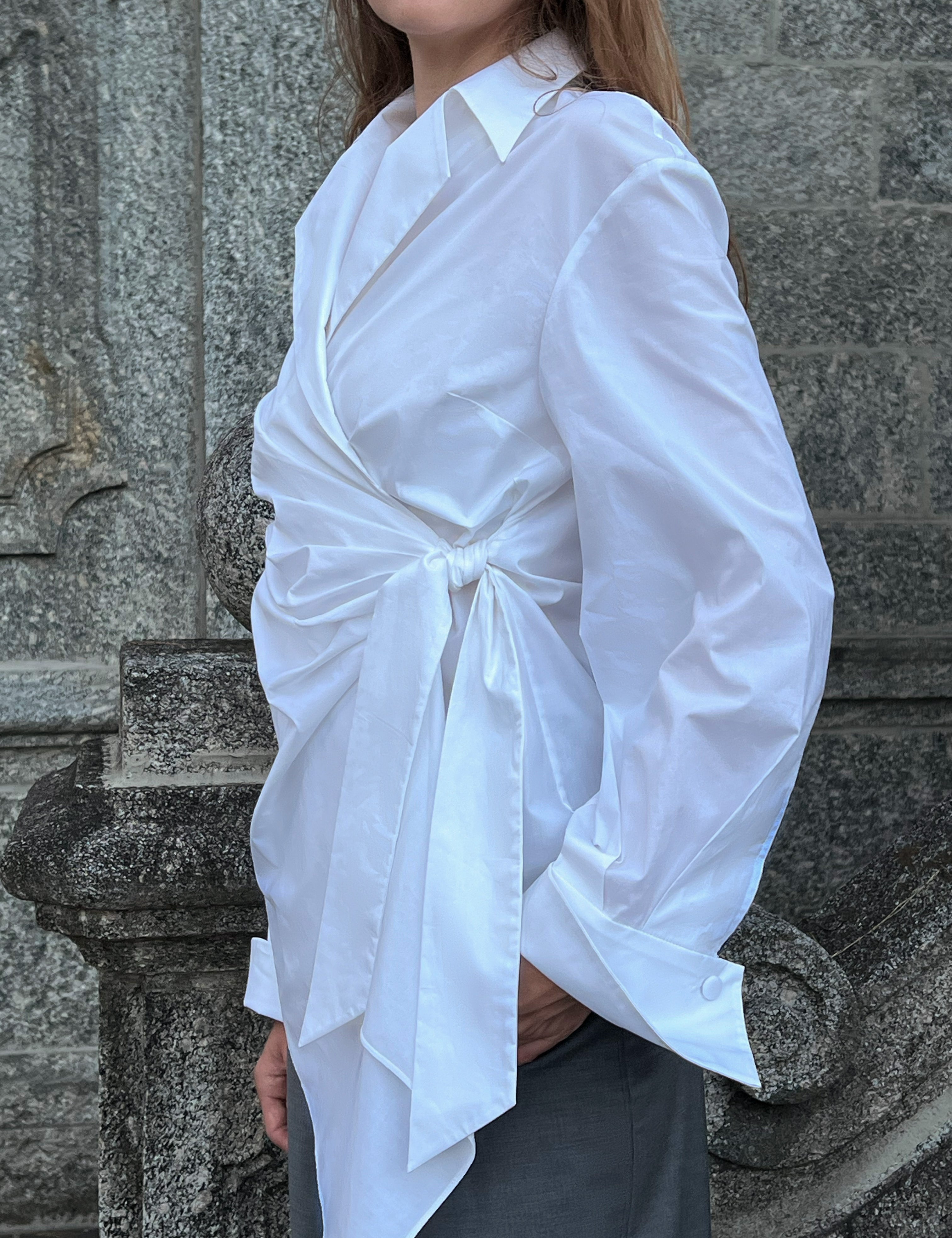 Side view of an architectural white cotton shirt showing its wrap construction and fluid silhouette.
