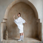 White open-back shirt worn by a model beneath a sand-toned arch, showcasing the signature drawstring back
