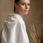 Side view of a model wearing a luxury white shirt with a signature split-back collar and elegant puff sleeves
