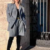 Woman in a gray suit and black boots standing against a stone wall
