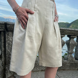 Tailored Bermuda shorts with front pleats and relaxed wide legs, worn by a model overlooking Lake Como