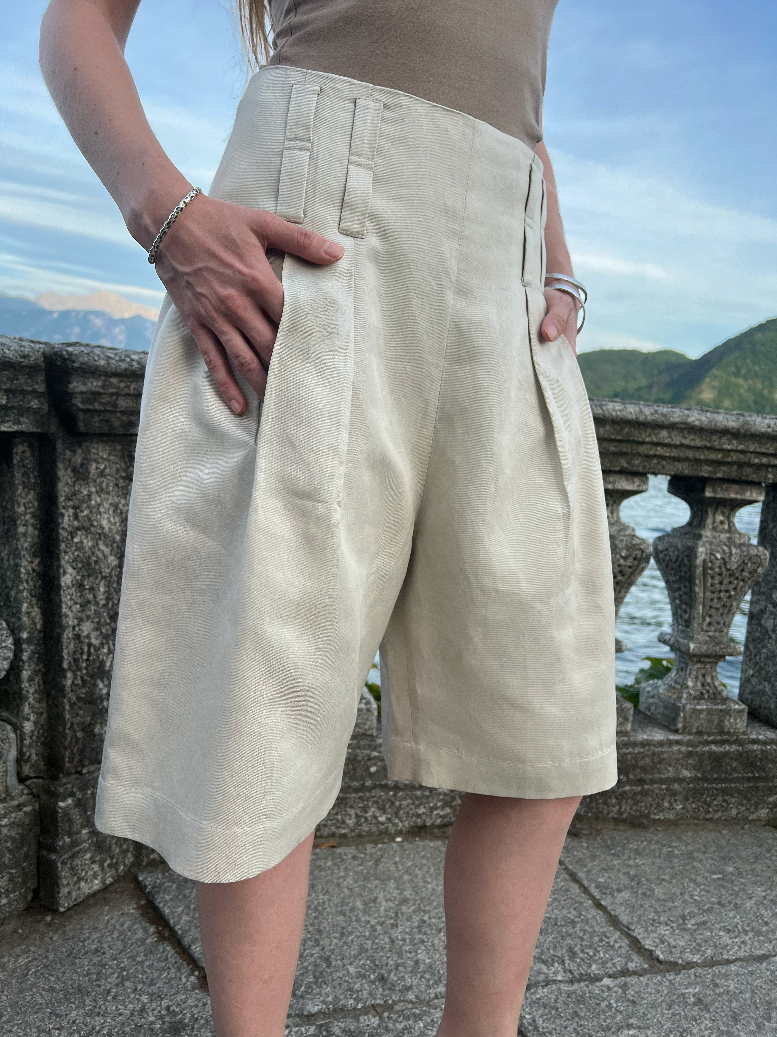 Tailored Bermuda shorts with front pleats and relaxed wide legs, worn by a model overlooking Lake Como
