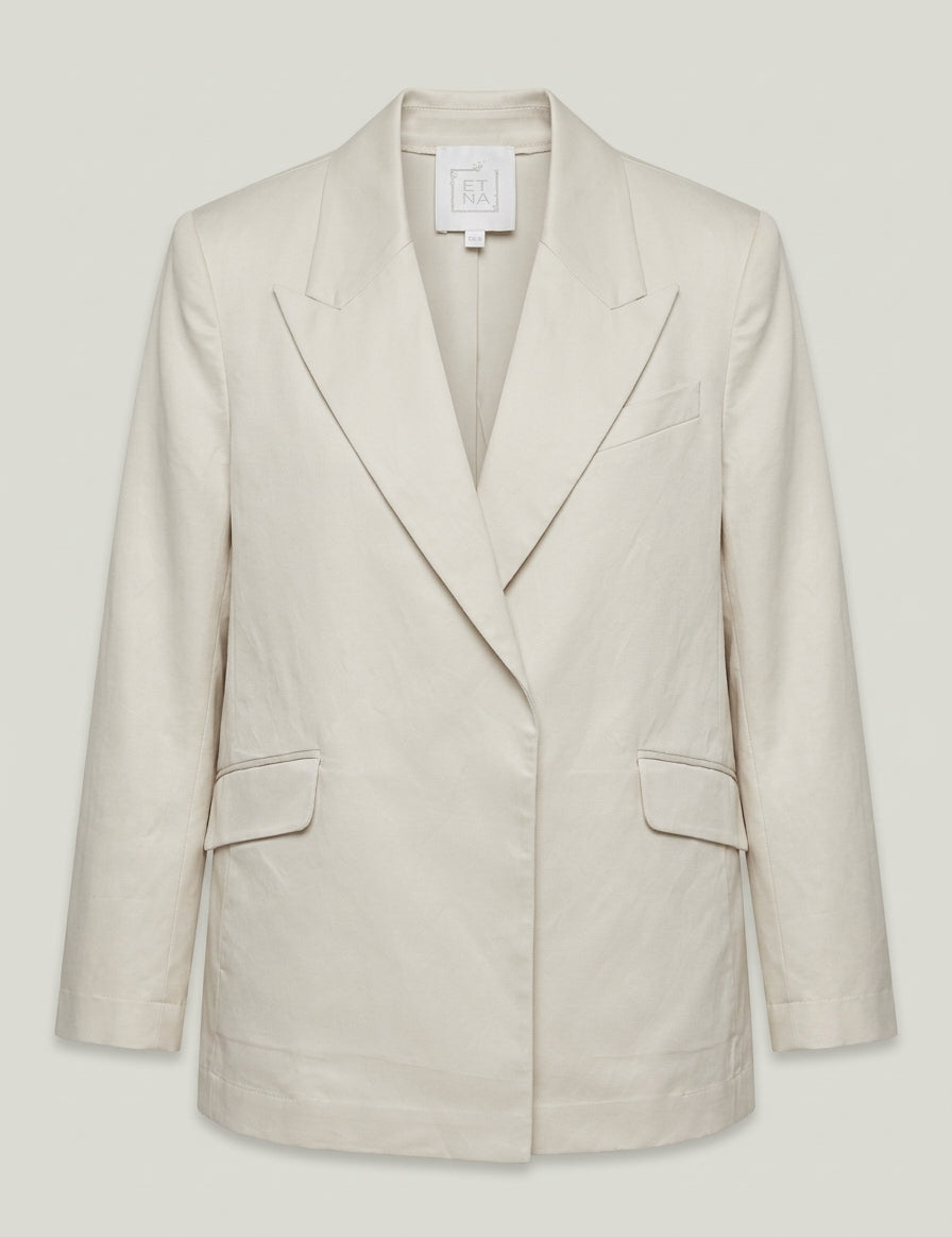 Product view of a tailored sand linen jacket with peaked lapels, structured shoulders and deep pockets.