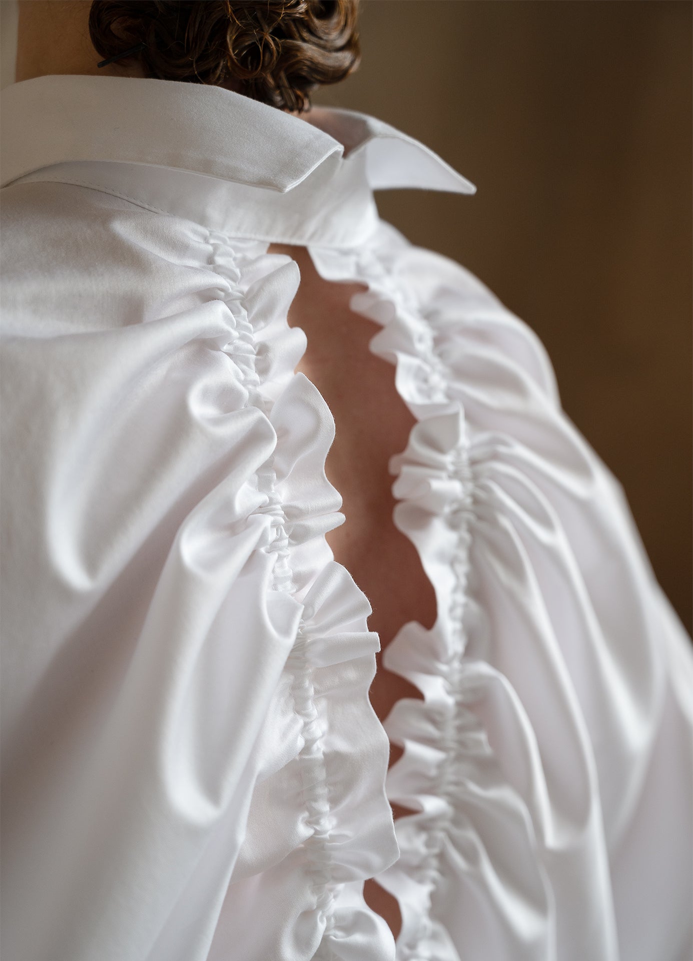 Sculptural white shirt worn by a model in a close-up back pose, showing the drawstrings and split collar