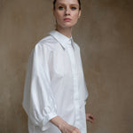 White puff-sleeve shirt worn by a model in a three-quarter front pose, showing its sculptural volume